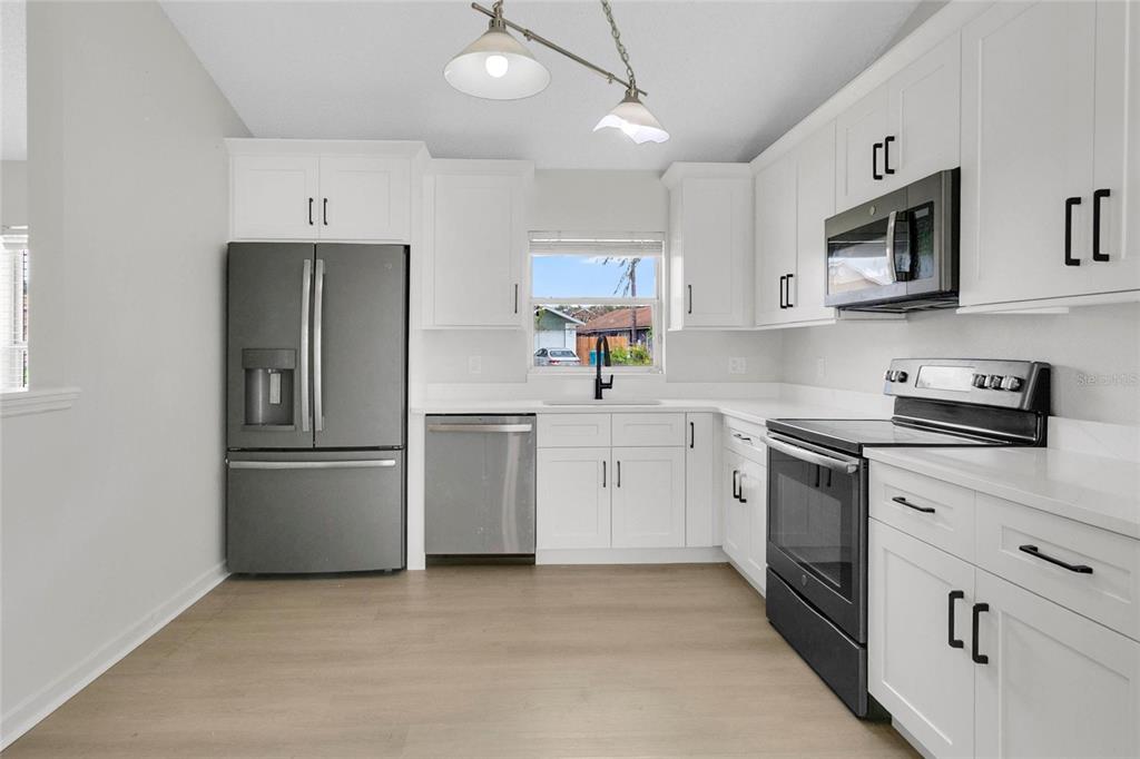 A kitchen features white cabinets, stainless steel appliances, and light wood-look flooring — 9703 RED CLOVER AVENUE, ORLANDO, FL