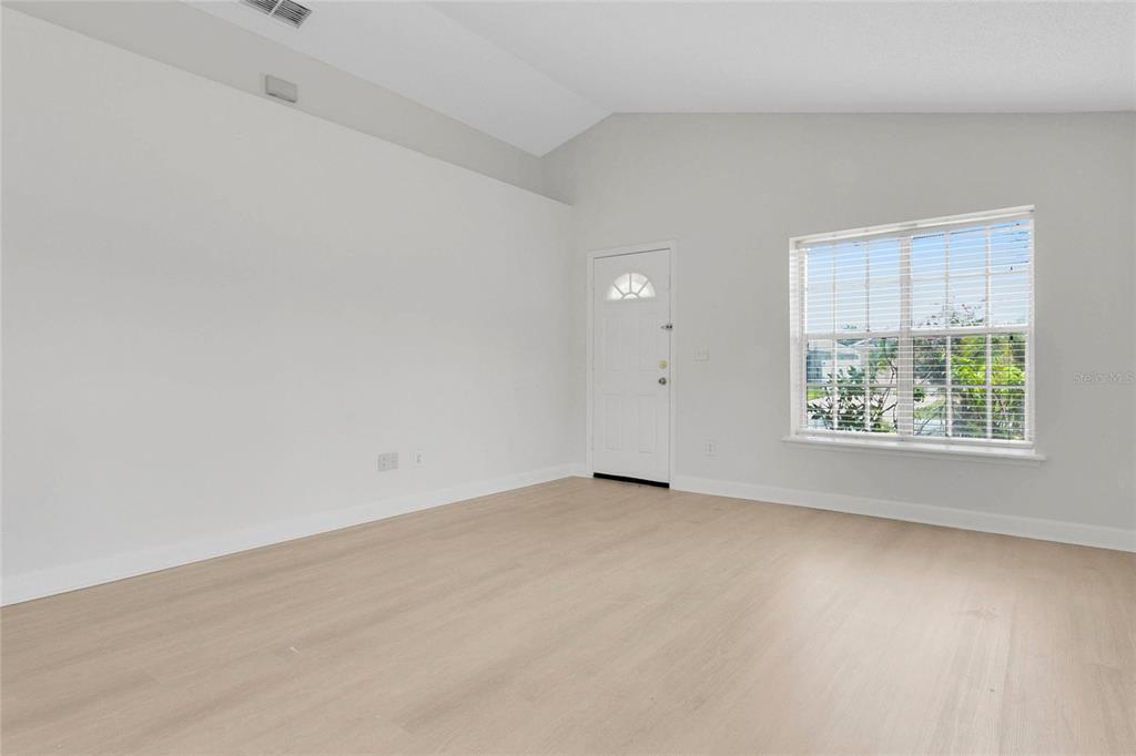 An empty room with light-colored wood flooring, white walls, a vaulted ceiling, and a window — 9703 RED CLOVER AVENUE, ORLANDO, FL
