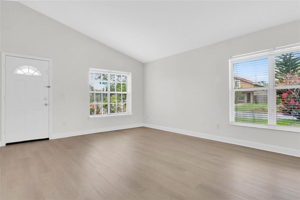 An empty room features light wood-look flooring, white walls, a vaulted ceiling, and two windows — 9703 RED CLOVER AVENUE, ORLANDO, FL