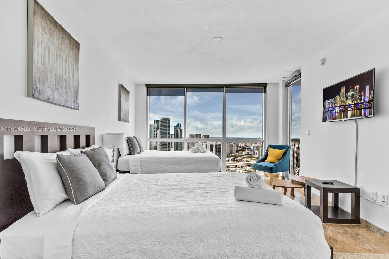 A bedroom features two beds, a blue accent chair, and floor-to-ceiling windows overlooking a city — 1750 N Bayshore Dr # 5014, Miami FL 33132, MIAMI, FL