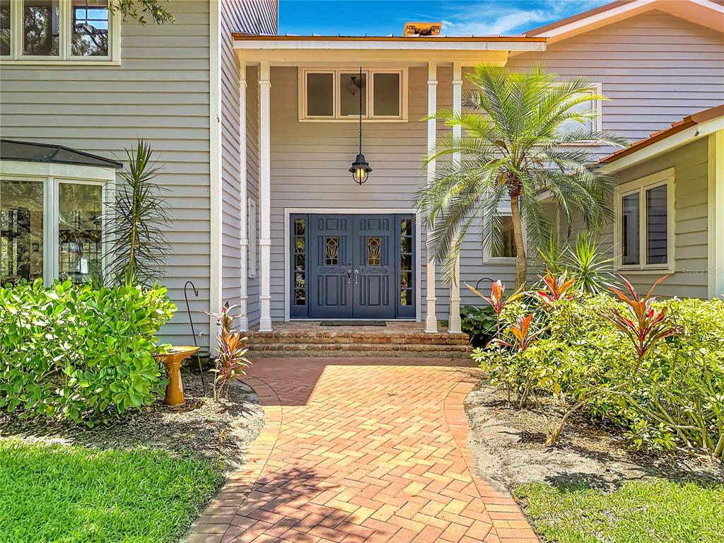 A brick walkway leads to the blue double front doors of a two-story house — 8005 17TH AVENUE W, BRADENTON, FL
