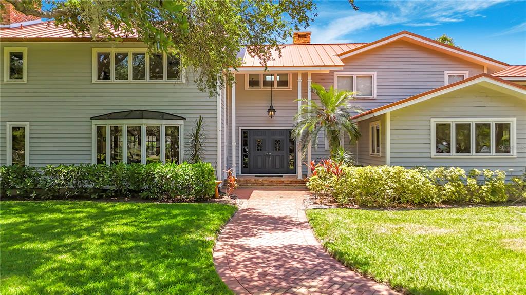 A two-story house with gray siding, a metal roof, and a brick walkway leading to the entrance — 8005 17TH AVENUE W, BRADENTON, FL