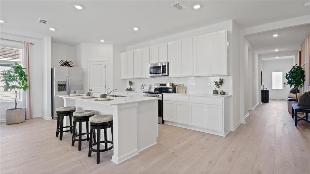 A modern kitchen features white cabinets, a central island with bar stools, and light flooring — 5551 GUAVA COURT, KISSIMMEE, FL