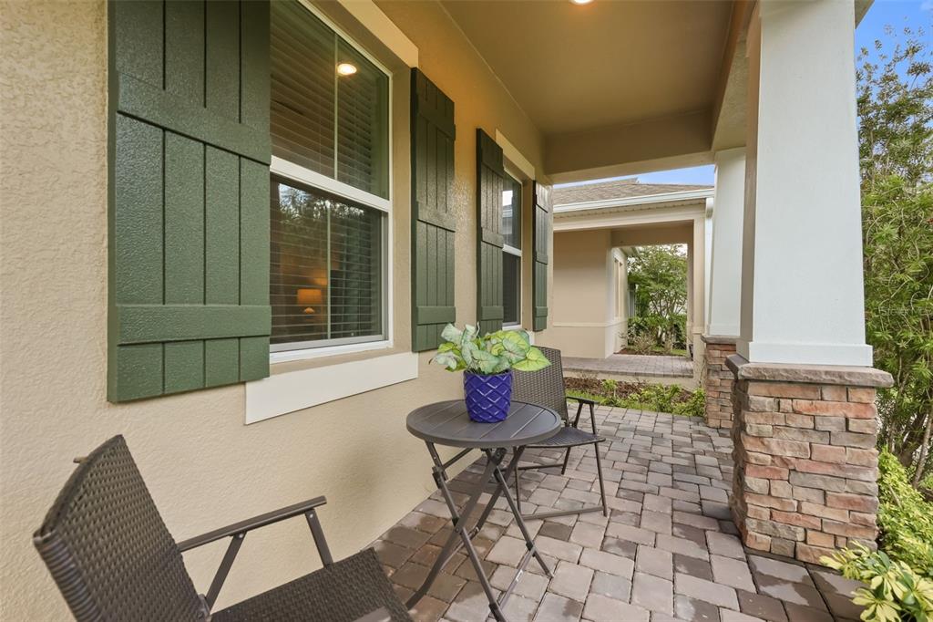 A covered front porch features stone columns, a small table with chairs, and green shutters — 620 BAYERN LANE, DEBARY, FL