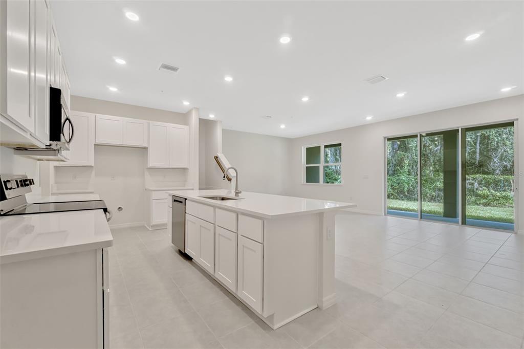 A modern kitchen features white cabinetry, a central island with a sink, and tile flooring — 5213 LUISA COURT, ST CLOUD, FL