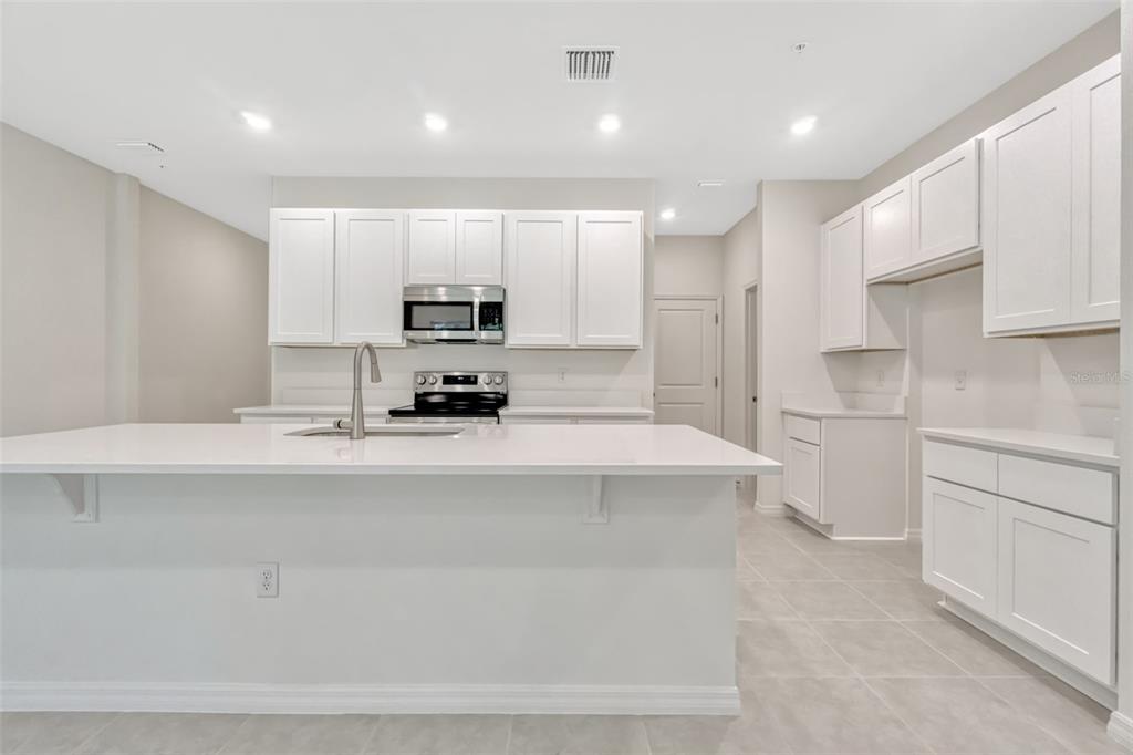 A modern kitchen features white cabinets, a large island with a sink, and tile flooring — 5213 LUISA COURT, ST CLOUD, FL