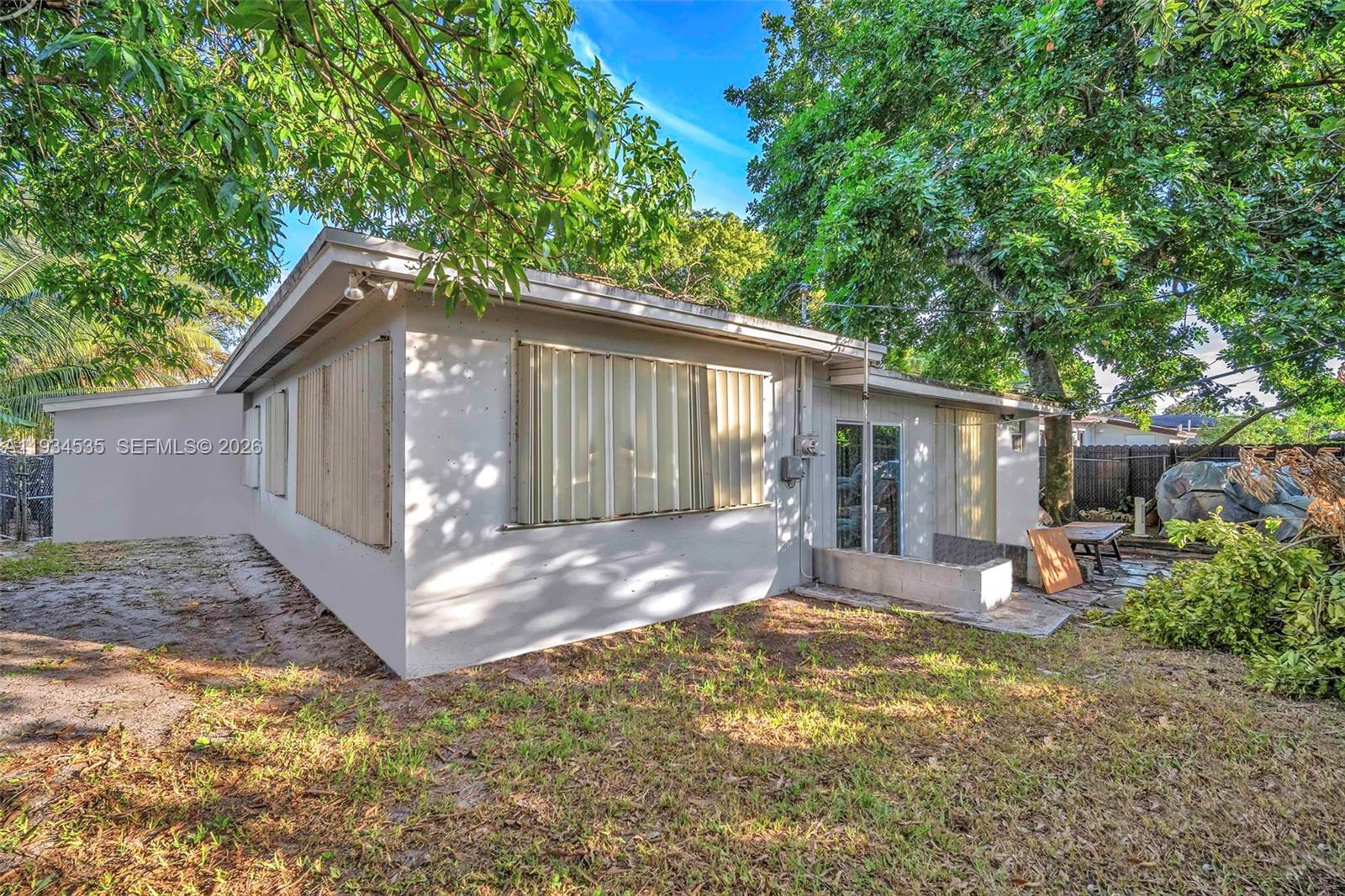 The exterior of a single-story house features light-colored walls, metal storm shutters, and trees — 16234 NE 9th Ct, North Miami Beach FL 33162, NORTH MIAMI BEACH, FL