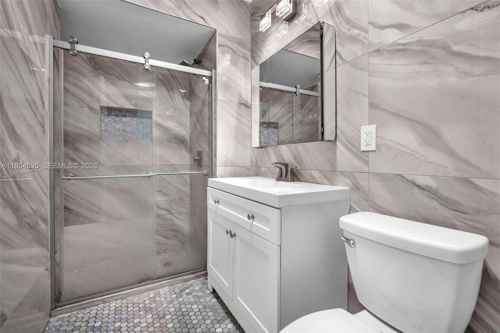 A modern bathroom features a glass-enclosed shower, white vanity, and marble-patterned wall tiles — 16234 NE 9th Ct, North Miami Beach FL 33162, NORTH MIAMI BEACH, FL