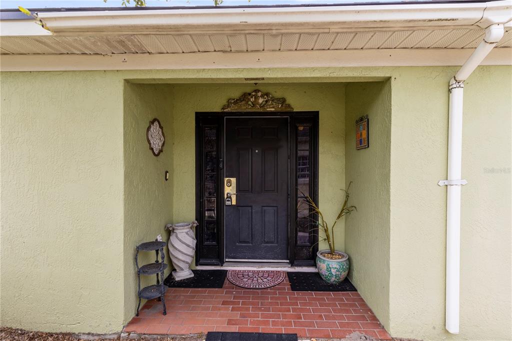 The front entrance features a black door with sidelights, a brick porch, and light green stucco — 1076 UNIVERSAL REST PLACE, KISSIMMEE, FL