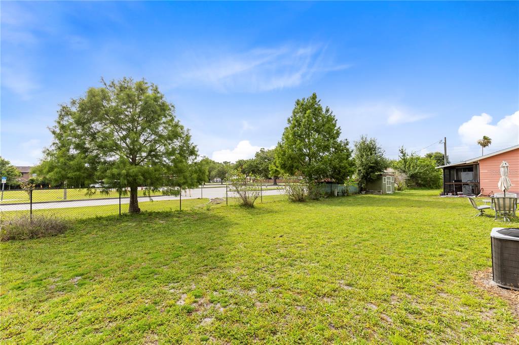 A grassy backyard features a chain-link fence, two large trees, and a small storage shed — 1076 UNIVERSAL REST PLACE, KISSIMMEE, FL