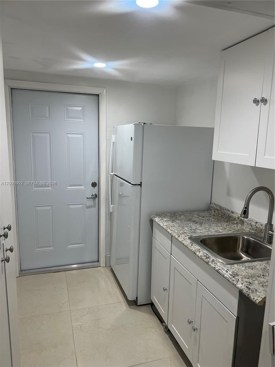 A small kitchen features white cabinets, a granite countertop, a stainless steel sink, and a refrigerator — 9945 SW 164th Ter # 1, Miami FL 33157, MIAMI, FL