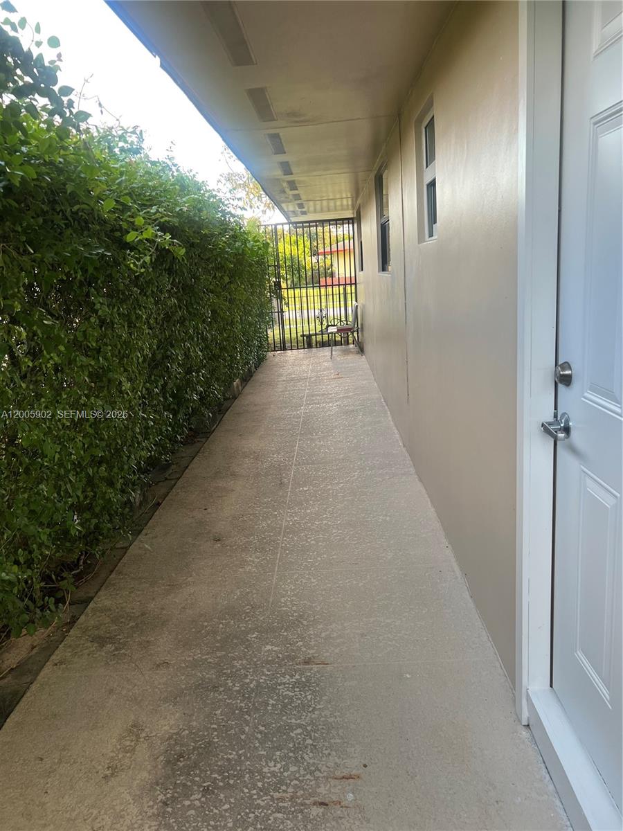 A concrete walkway runs along the side of a building next to a tall hedge — 9945 SW 164th Ter # 1, Miami FL 33157, MIAMI, FL