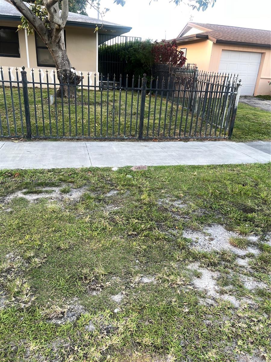 A metal fence encloses the front yard of a single-story house with a tree — 9945 SW 164th Ter # 1, Miami FL 33157, MIAMI, FL
