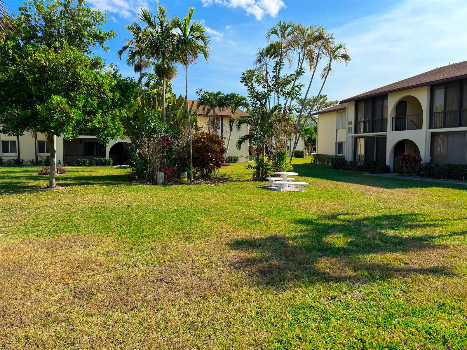 A grassy courtyard features a small white picnic table surrounded by palm trees and apartments — 3530 Pine Needle Drive # 2, FL 33463, FL