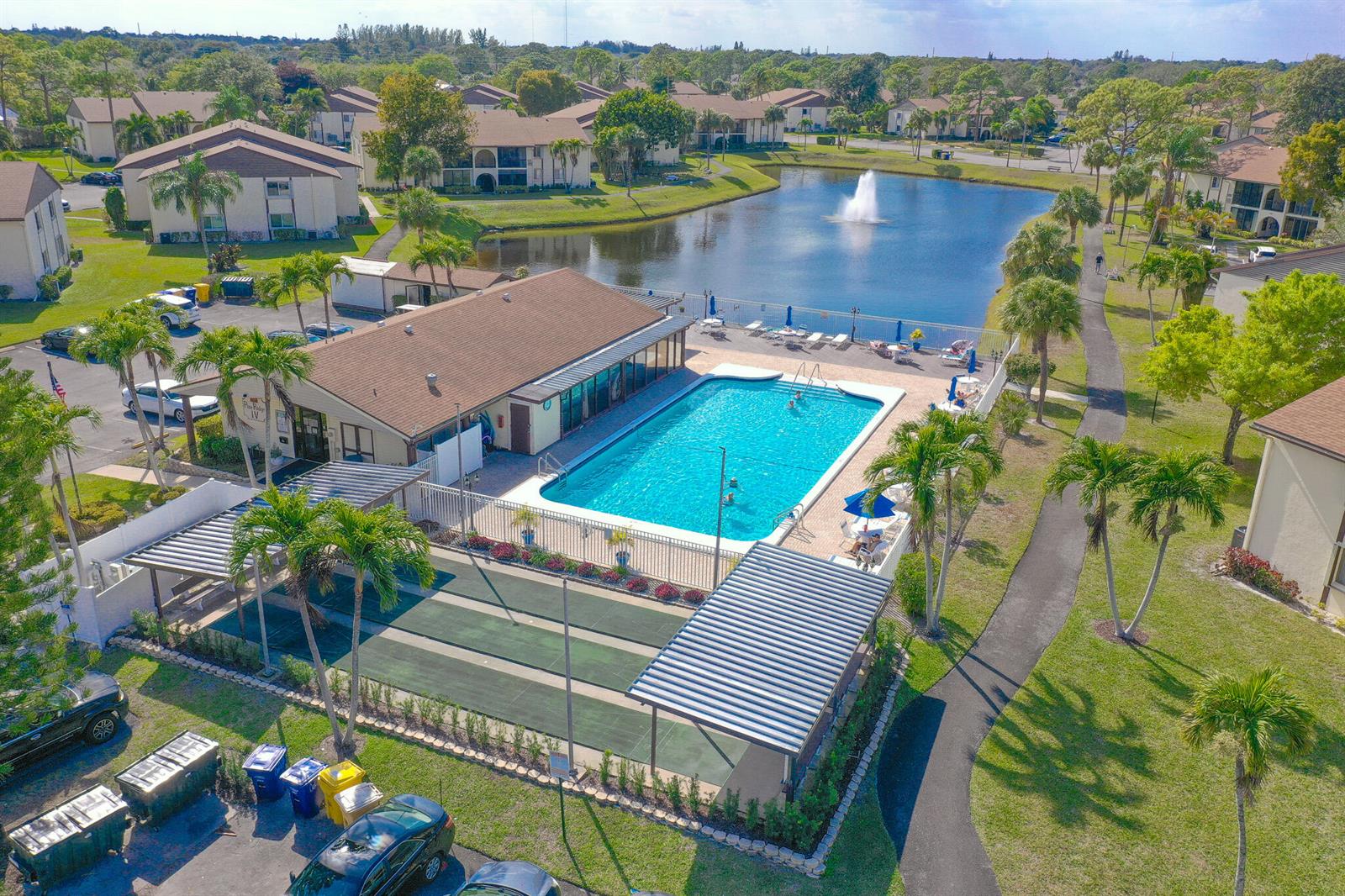 An aerial view shows a swimming pool, shuffleboard courts, and a pond at a residential complex — 3530 Pine Needle Drive # 2, FL 33463, FL