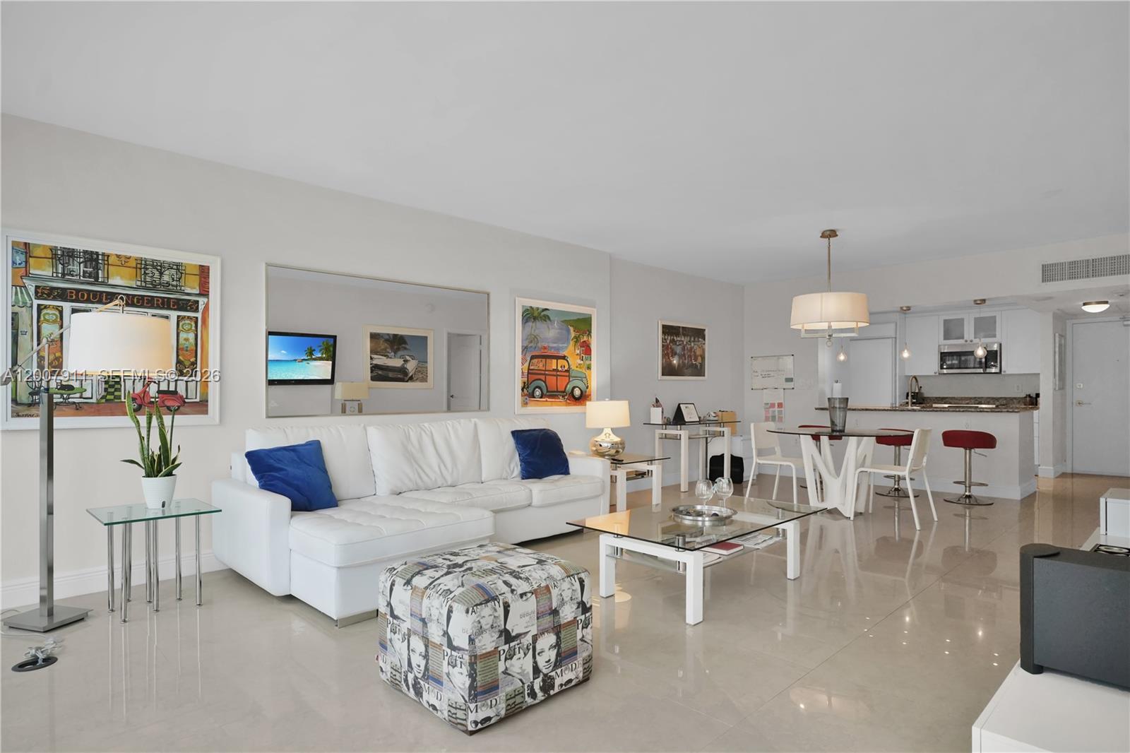 A bright living room features a white sectional sofa, glass coffee table, and open kitchen — 10275 Collins Ave # 315, Bal Harbour FL 33154, BAL HARBOUR, FL