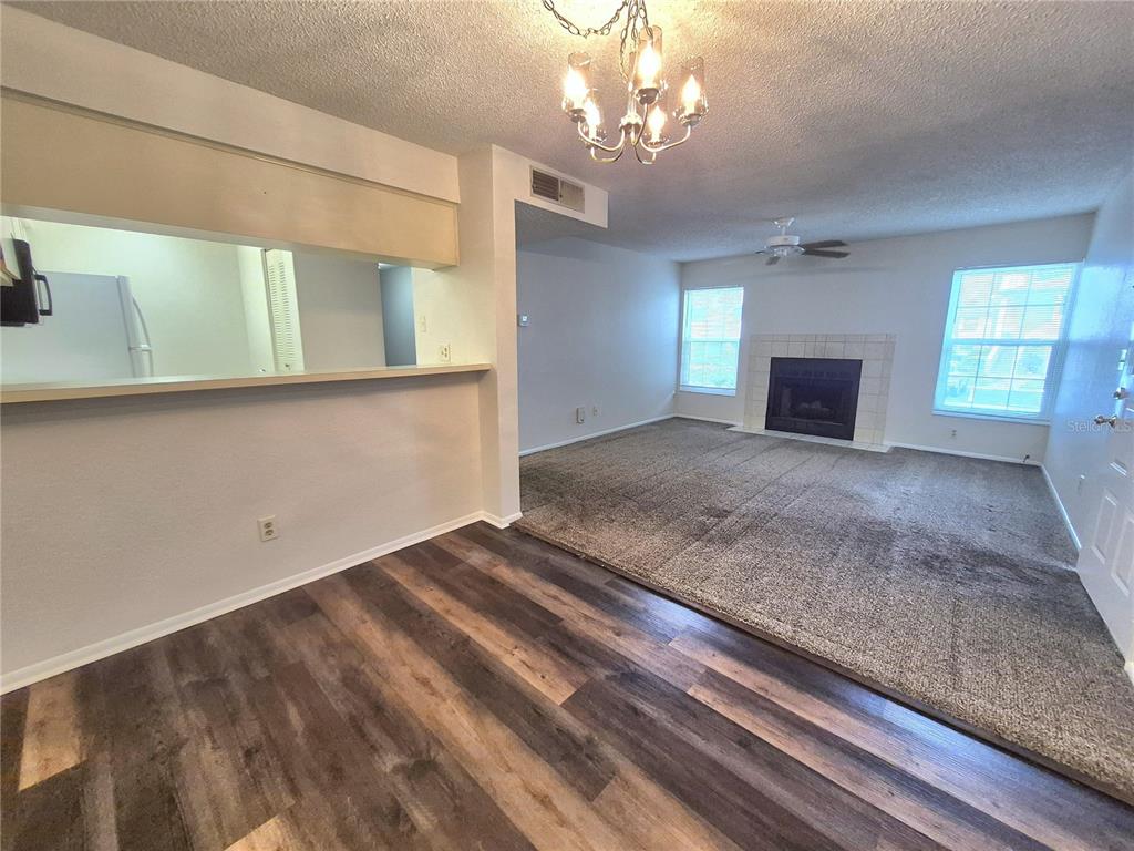 A living room with carpeted flooring and a fireplace connects to a kitchen breakfast bar — 3025 BONAVENTURE CIRCLE UNIT 101, PALM HARBOR, FL