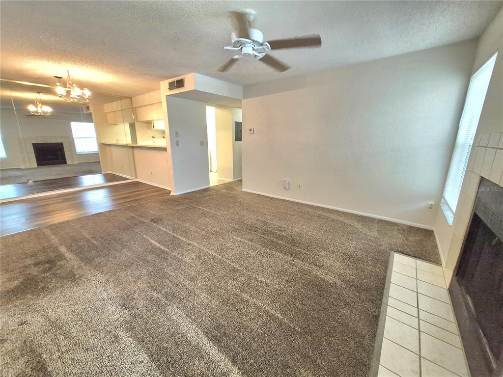 A living room with carpeted flooring, a ceiling fan, and a fireplace with tile hearth — 3025 BONAVENTURE CIRCLE UNIT 101, PALM HARBOR, FL