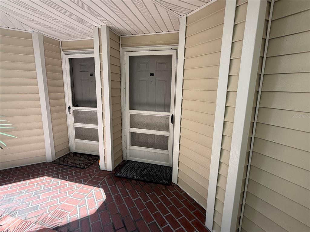 Two exterior doors with screen doors and welcome mats sit on a red brick patio — 3900 SOUTHPOINTE DRIVE UNIT 120, ORLANDO, FL