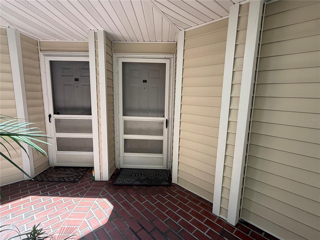 Two exterior doors with screen doors and welcome mats sit on a brick patio — 3900 SOUTHPOINTE DRIVE UNIT 120, ORLANDO, FL