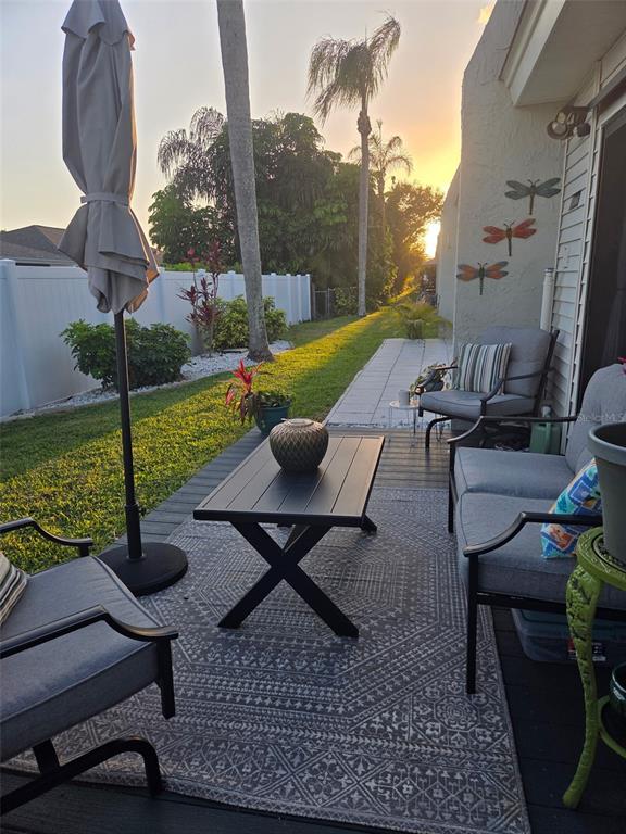 A patio with outdoor furniture, a rug, and a table overlooks a grassy backyard at sunset — 13830 MISSION OAKS BOULEVARD UNIT 13830, SEMINOLE, FL