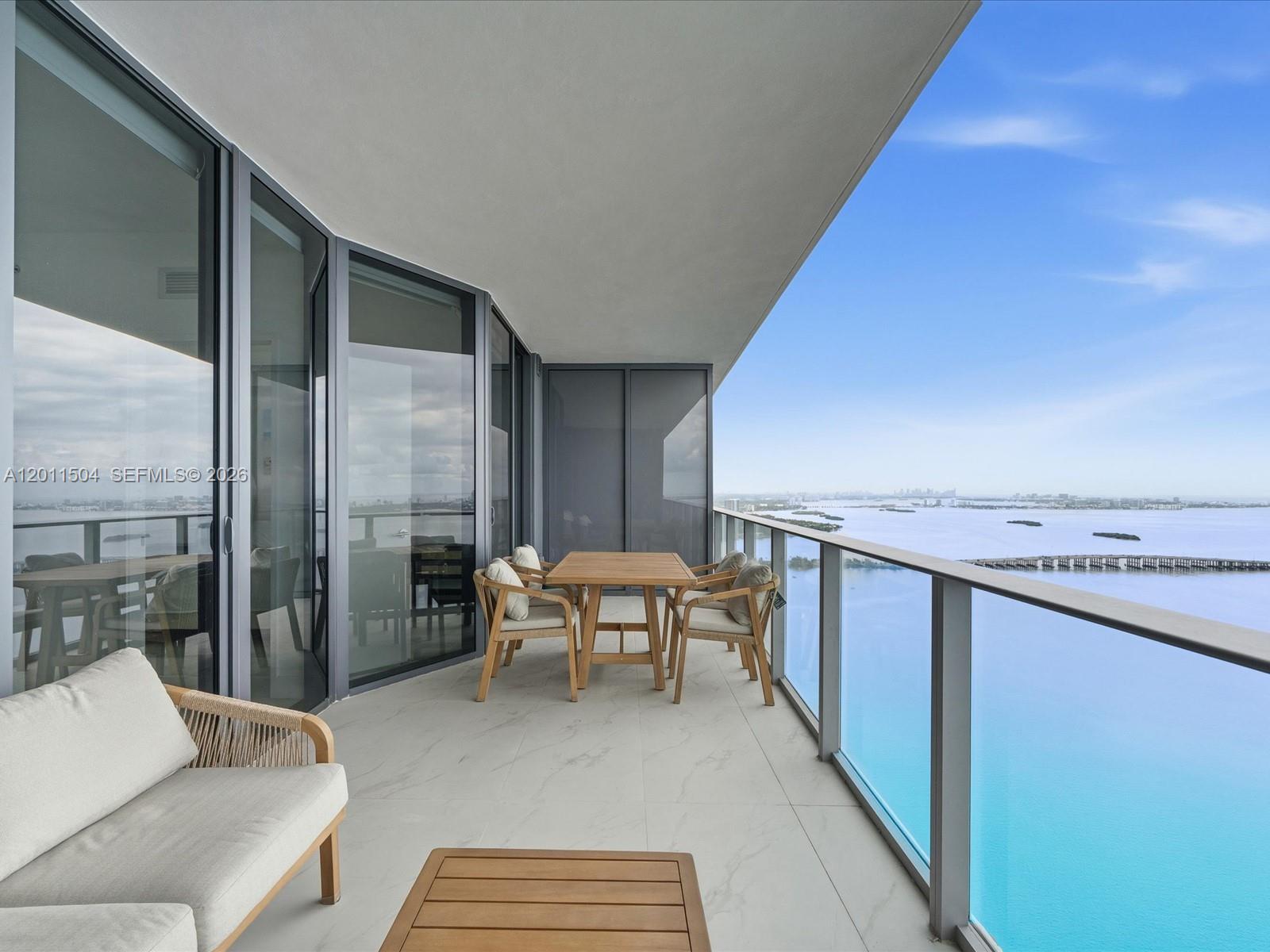 A balcony with outdoor furniture overlooks a large body of water and a distant city — 700 NE 24th Street # 4606, Miami FL 33137, MIAMI, FL