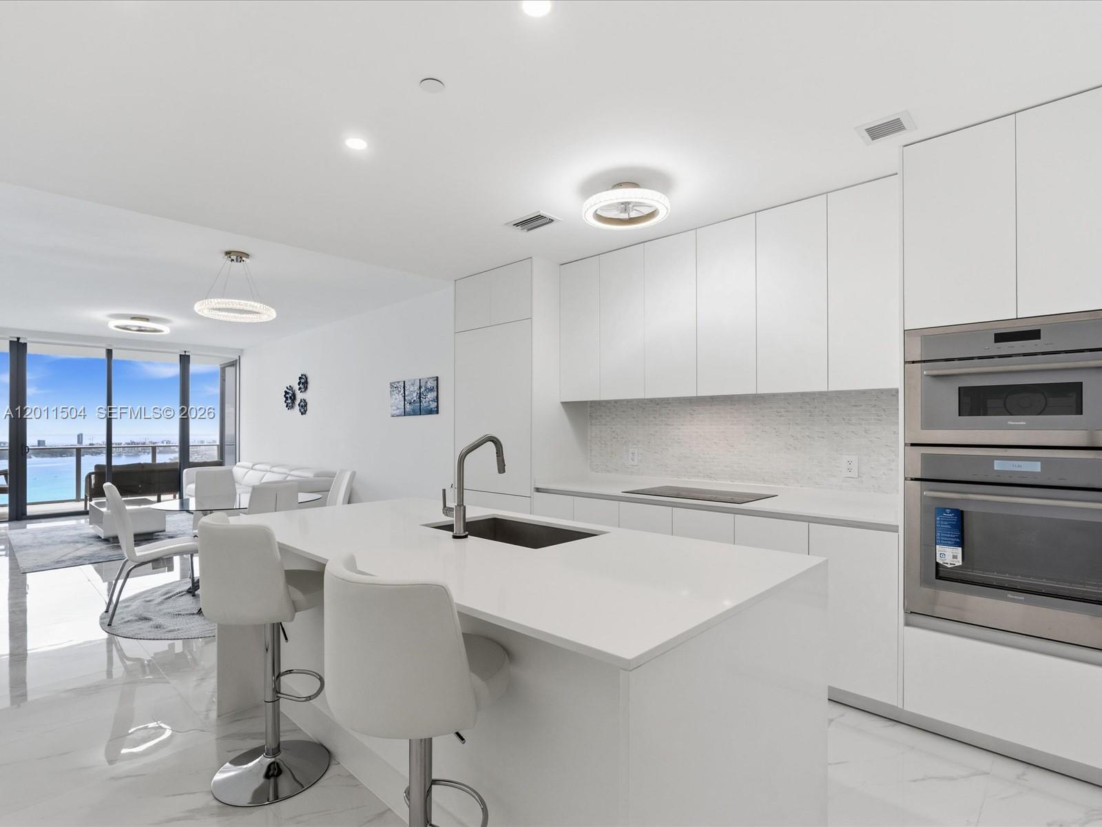 A modern white kitchen features a central island, stainless steel appliances, and a water view — 700 NE 24th Street # 4606, Miami FL 33137, MIAMI, FL