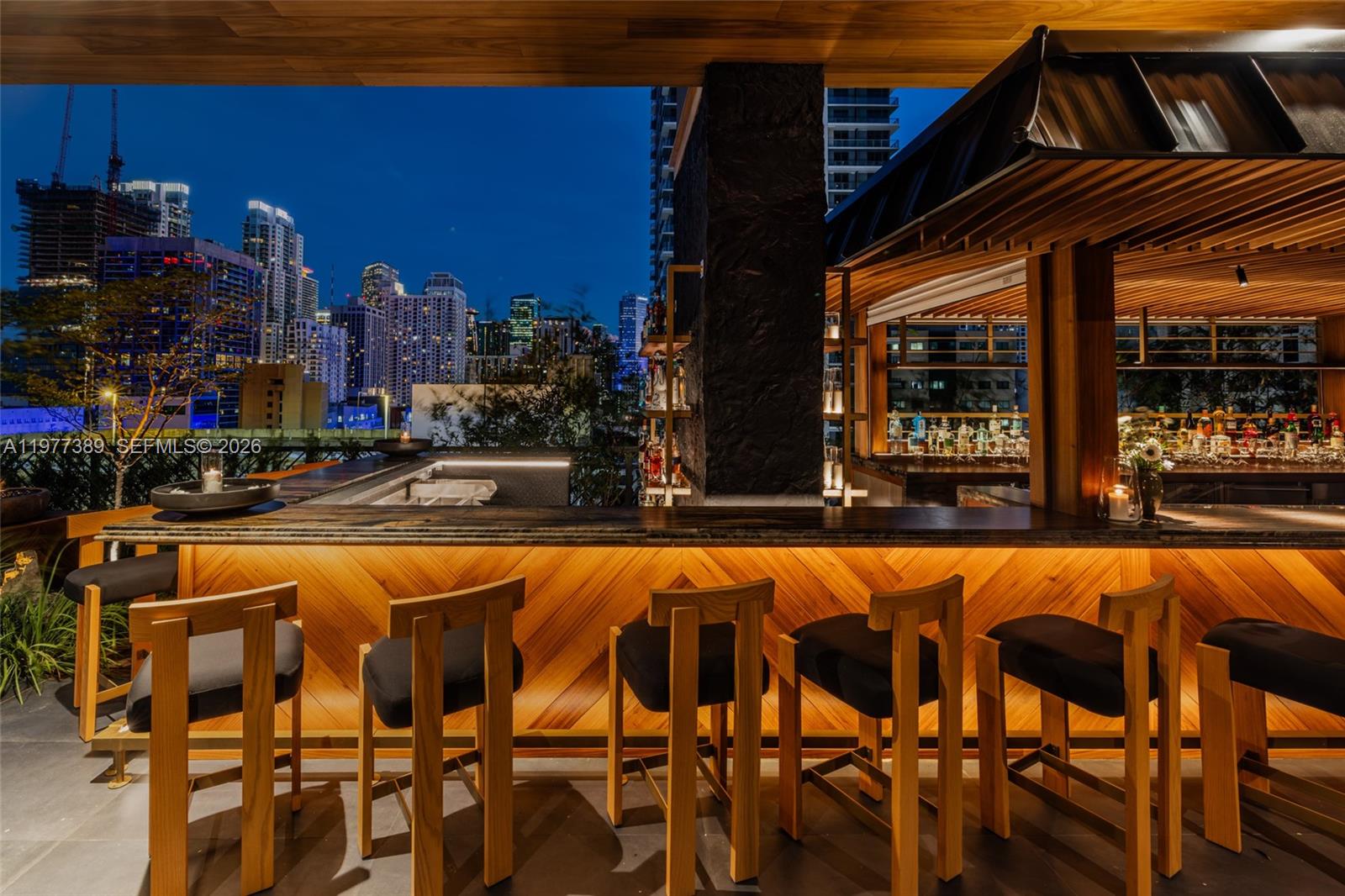 An outdoor bar with wooden stools and chevron paneling overlooks a city skyline at night — 159 NE 6th St # 3713, Miami FL 33132, MIAMI, FL