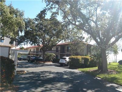 A multi-story apartment building with a parking lot and large trees in the foreground — 6268 PALMA DEL MAR BOULEVARD S UNIT 111, ST PETERSBURG, FL