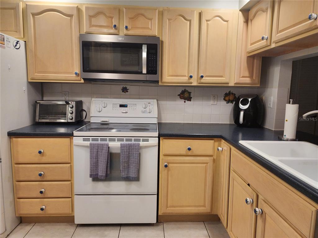 A kitchen features light wood cabinets, dark countertops, white appliances, and a tiled backsplash — 6268 PALMA DEL MAR BOULEVARD S UNIT 111, ST PETERSBURG, FL