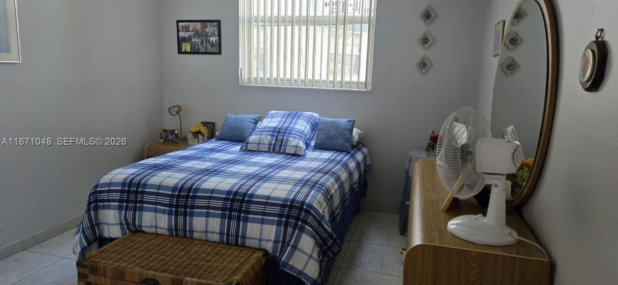 A bedroom features a plaid bedspread, a window with vertical blinds, and a white fan — 1913 S Ocean Dr # 138, Hallandale Beach FL 33009, HALLANDALE BEACH, FL