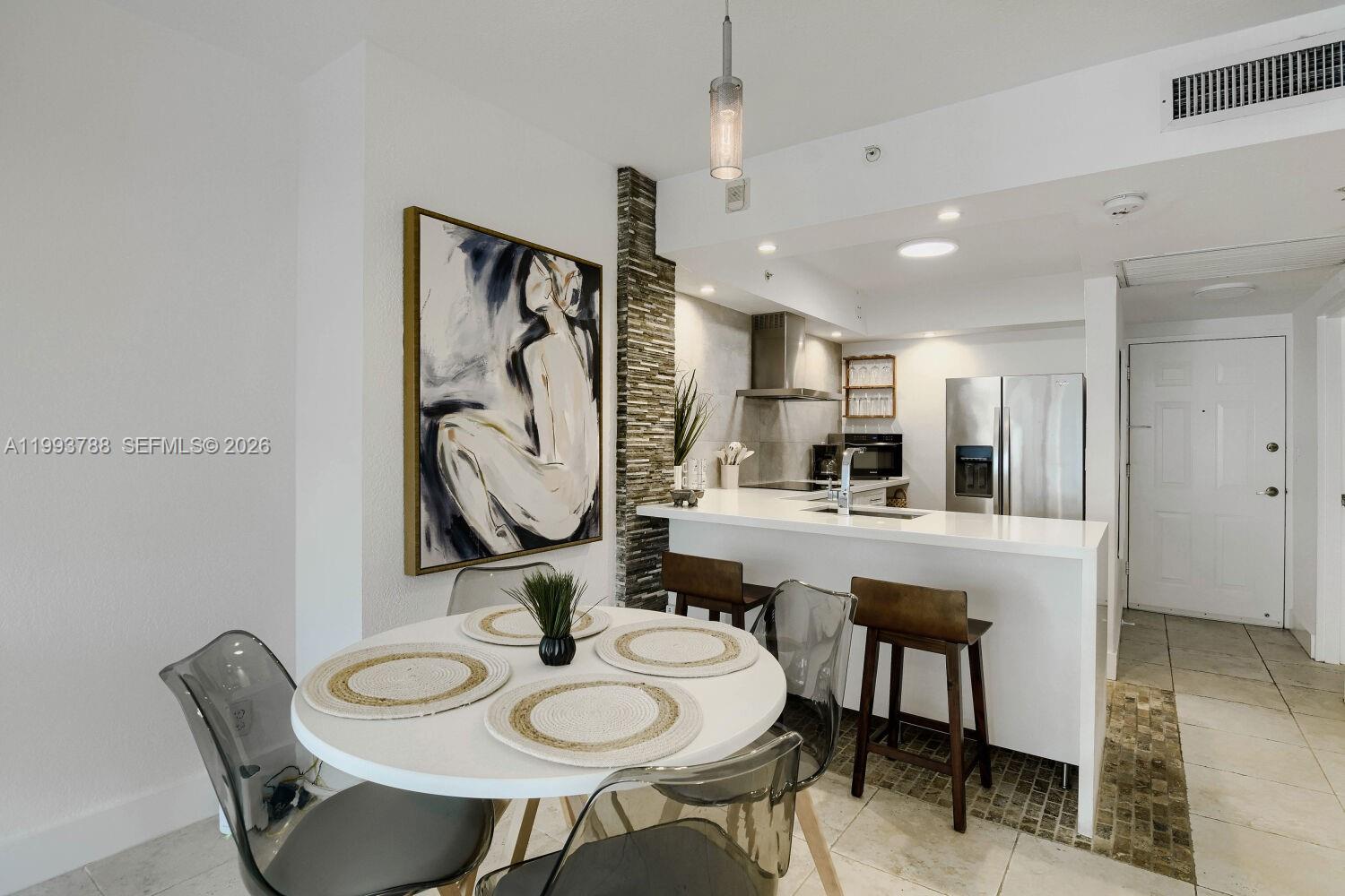A dining area with a round table sits adjacent to a modern kitchen with bar seating — 2501 S Ocean Dr, Hollywood FL 33019, HOLLYWOOD, FL