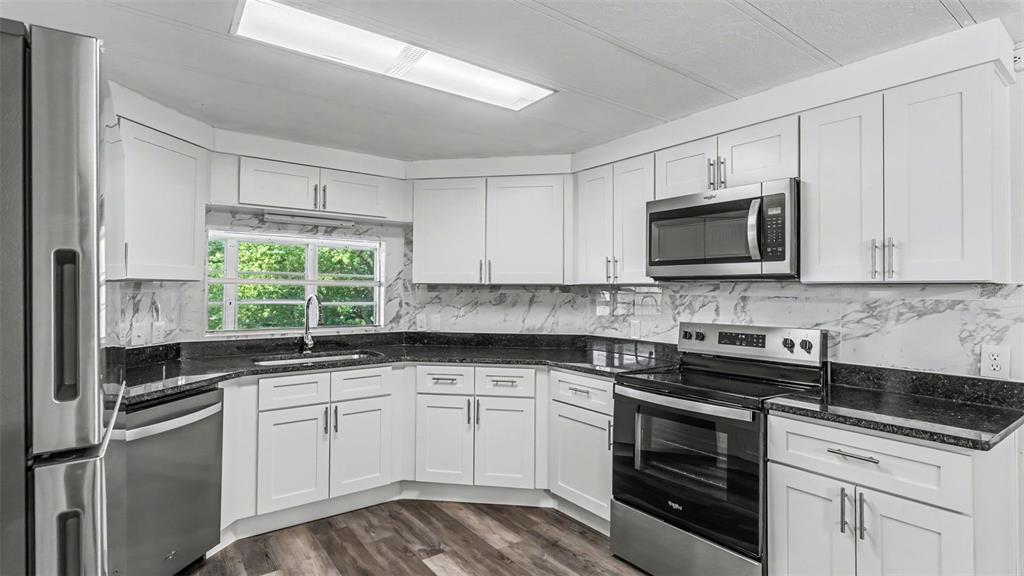 A kitchen features white cabinets, stainless steel appliances, dark countertops, and a marble-patterned backsplash — 2055 S FLORAL AVENUE UNIT 324, BARTOW, FL