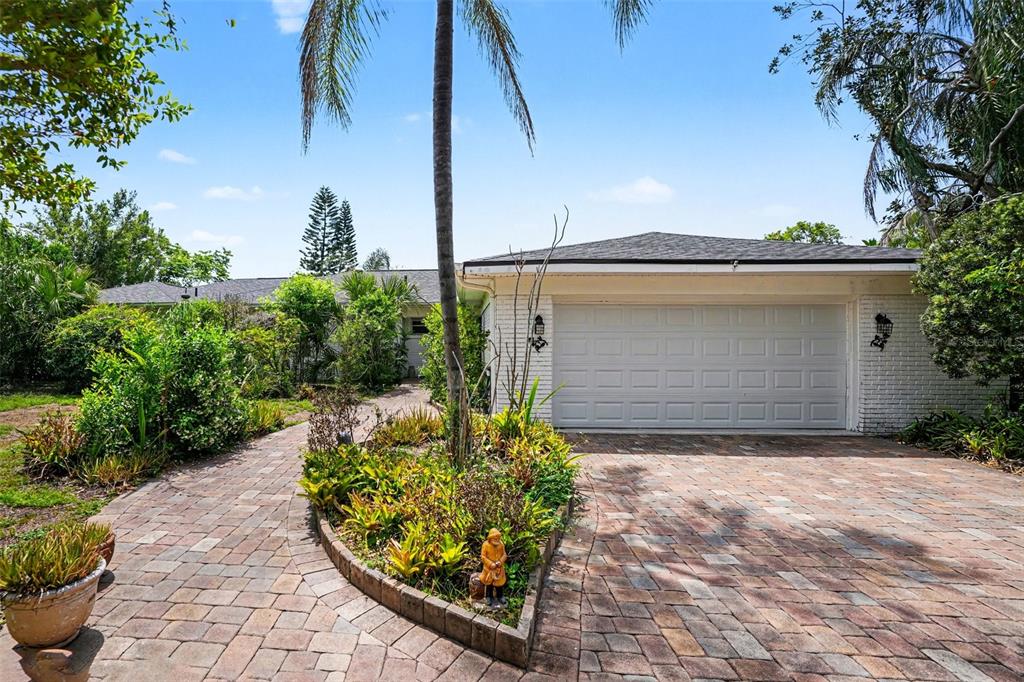 A white brick house features a paved driveway, a landscaped garden, and a palm tree — 1350 ECKLES DRIVE, TAMPA, FL