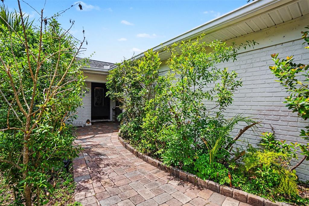 A brick walkway leads to the front entrance of a white brick house with landscaping — 1350 ECKLES DRIVE, TAMPA, FL