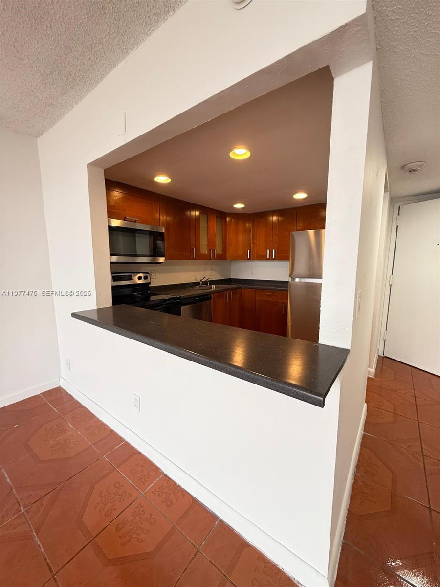 A kitchen with wood cabinets and stainless steel appliances is viewed over a breakfast bar — 13499 Biscayne Blvd # 1114, North Miami FL 33181, NORTH MIAMI, FL