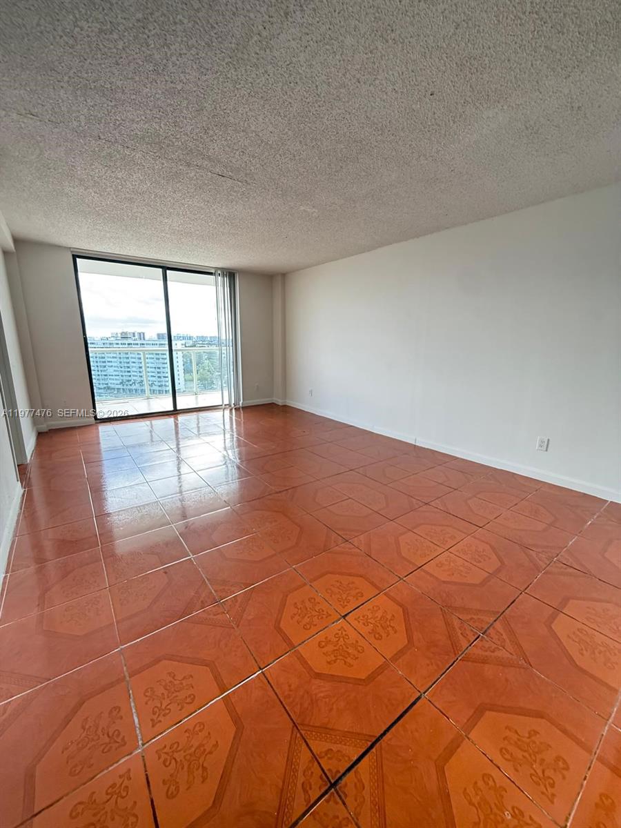 An empty room features orange patterned tile flooring, white walls, and a sliding glass balcony door — 13499 Biscayne Blvd # 1114, North Miami FL 33181, NORTH MIAMI, FL
