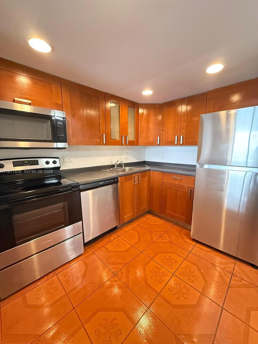 A kitchen features wood cabinets, stainless steel appliances, and orange patterned tile flooring — 13499 Biscayne Blvd # 1114, North Miami FL 33181, NORTH MIAMI, FL