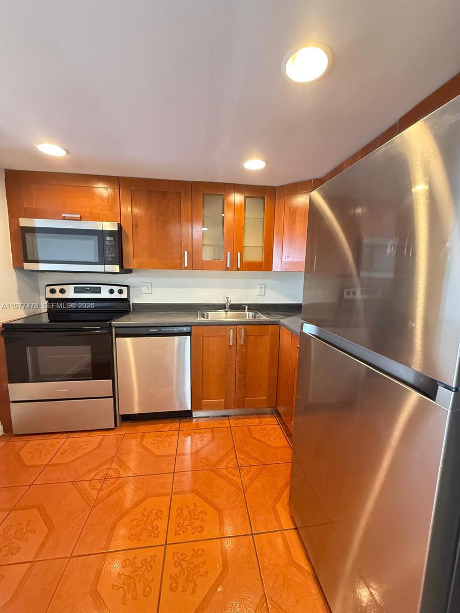 A kitchen features wooden cabinets, stainless steel appliances, and orange patterned floor tiles — 13499 Biscayne Blvd # 1114, North Miami FL 33181, NORTH MIAMI, FL