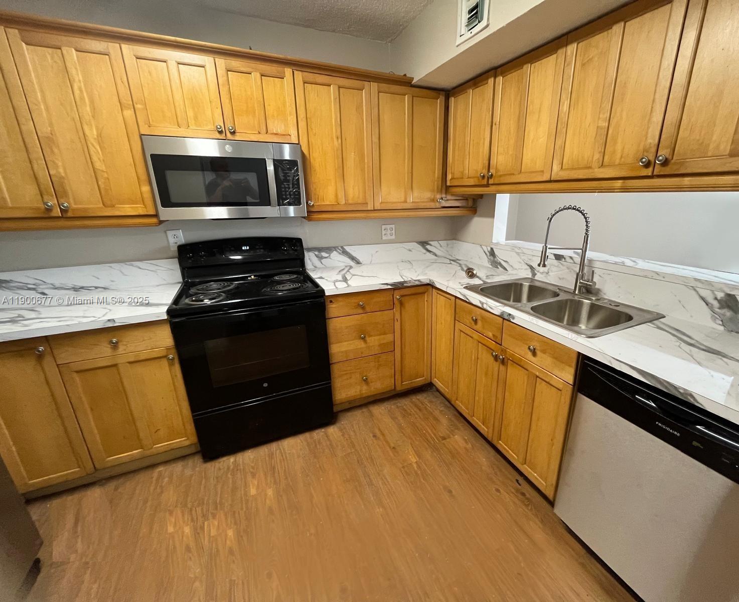 A kitchen features wood cabinets, black appliances, and white marble-patterned countertops — 3400 Foxcroft Rd # 115, Miramar FL 33025, MIRAMAR, FL