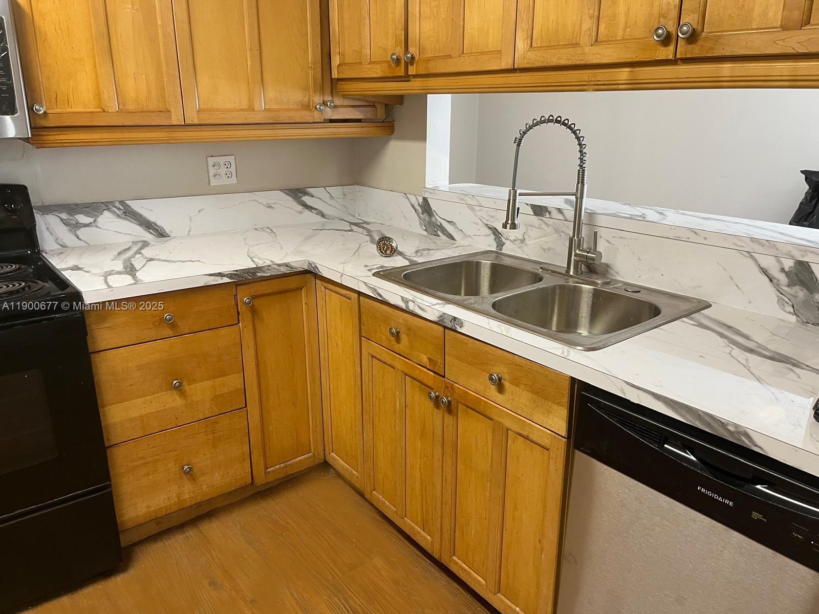 A kitchen features wooden cabinets, a marble-patterned countertop, a double sink, and black appliances — 3400 Foxcroft Rd # 115, Miramar FL 33025, MIRAMAR, FL