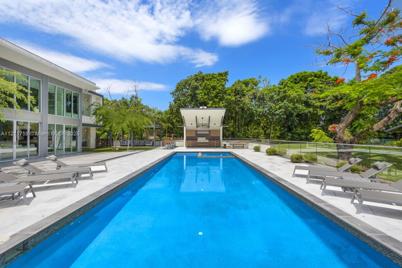 A modern backyard features a rectangular swimming pool, lounge chairs, and a covered outdoor kitchen — 14305 Stirling Rd, Southwest Ranches FL 33330, SOUTHWEST RANCHES, FL