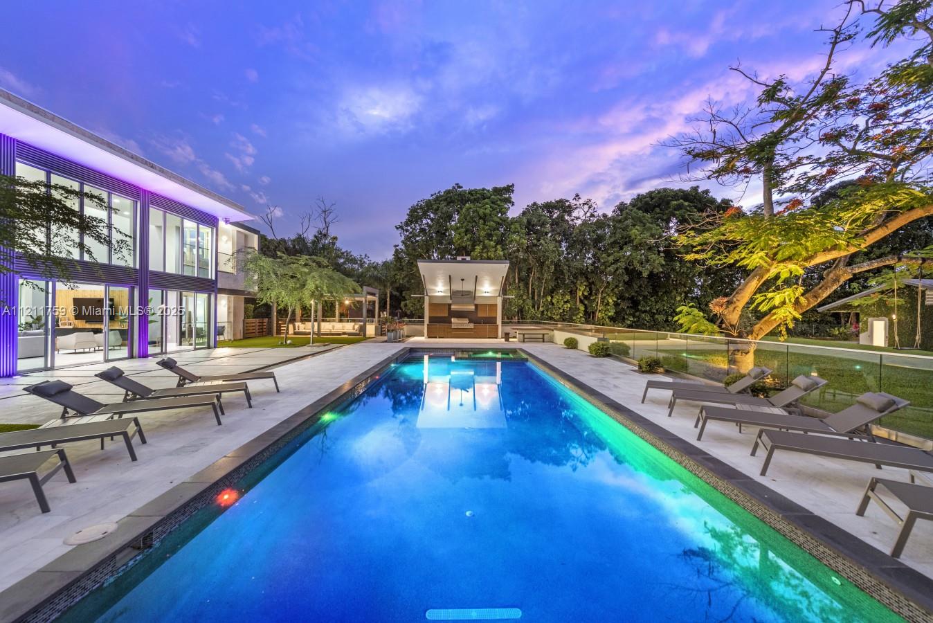 A modern house exterior features a rectangular swimming pool, lounge chairs, and an outdoor kitchen — 14305 Stirling Rd, Southwest Ranches FL 33330, SOUTHWEST RANCHES, FL