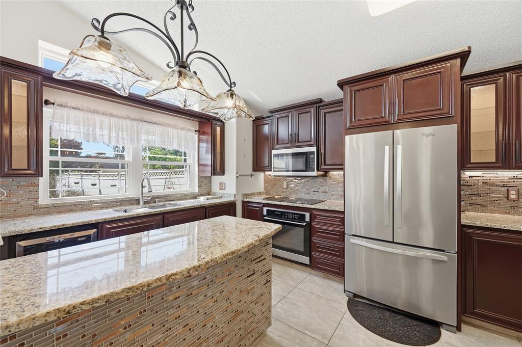 A kitchen features dark wood cabinets, granite countertops, stainless steel appliances, and a tiled island — 12315 KENTON COURT, ORLANDO, FL