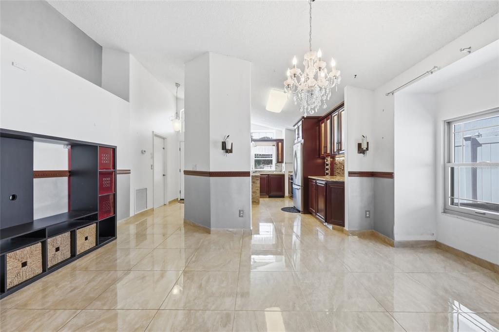 A bright, open-concept room features glossy tile floors, a crystal chandelier, and dark wood cabinetry — 12315 KENTON COURT, ORLANDO, FL