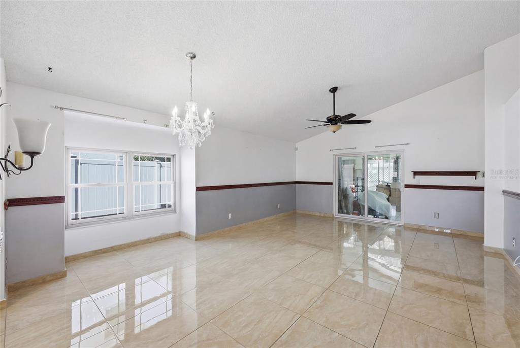 A bright, empty room features large beige floor tiles, a chandelier, and a ceiling fan — 12315 KENTON COURT, ORLANDO, FL