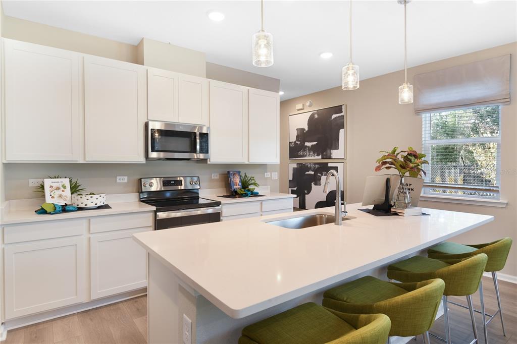 A modern kitchen features white cabinets, a quartz island with green stools, and stainless appliances — 2525 29TH LANE E, PALMETTO, FL