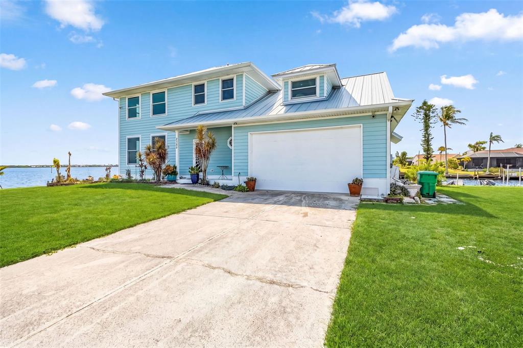 A light blue two-story house with a metal roof and a concrete driveway sits waterfront — 2380 VANCE TERRACE, PORT CHARLOTTE, FL