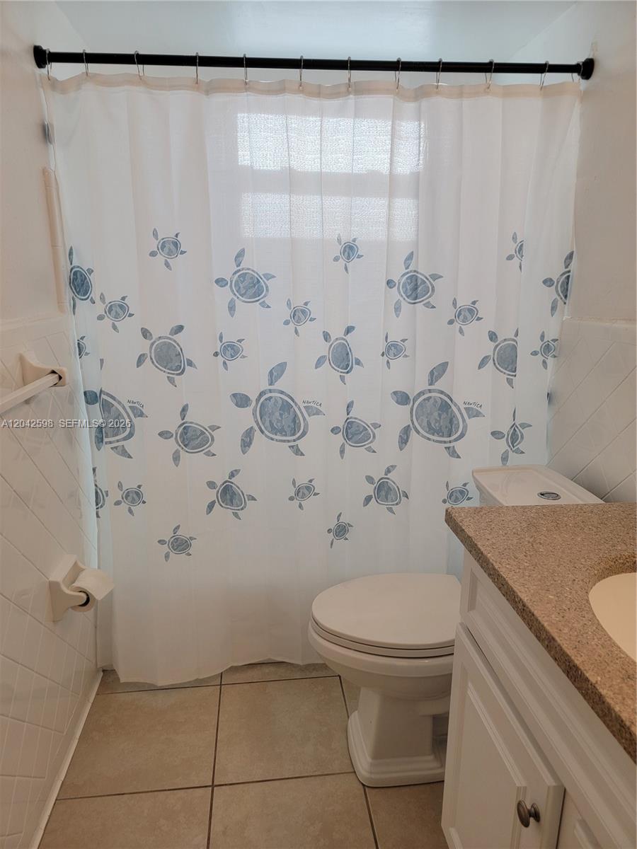 A bathroom features a white toilet, a vanity with a stone countertop, and a turtle-patterned shower curtain — 835 Lenox Ave # 102, Miami Beach FL 33139, MIAMI BEACH, FL