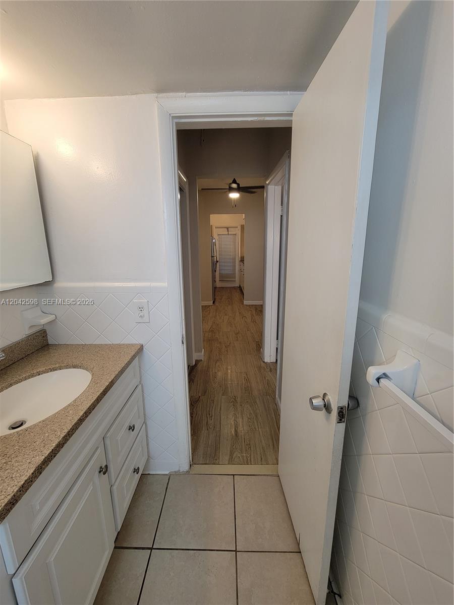 A bathroom with a vanity and tiled walls opens into a hallway with wood flooring — 835 Lenox Ave # 102, Miami Beach FL 33139, MIAMI BEACH, FL